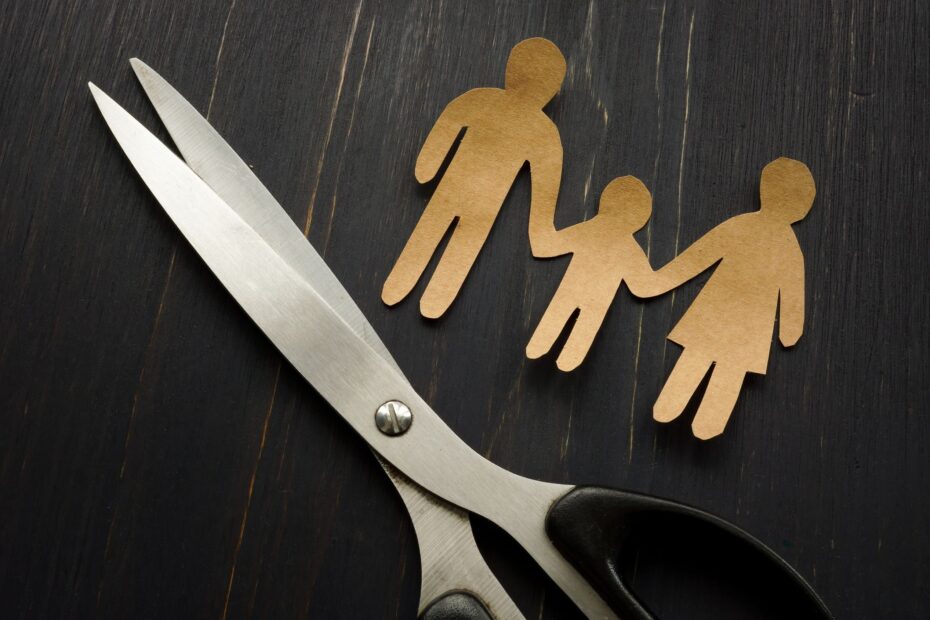 na obrazku są nożyczki oraz papierowe postaci mężczyzny dziecka i kobiety trzymających się za ręce